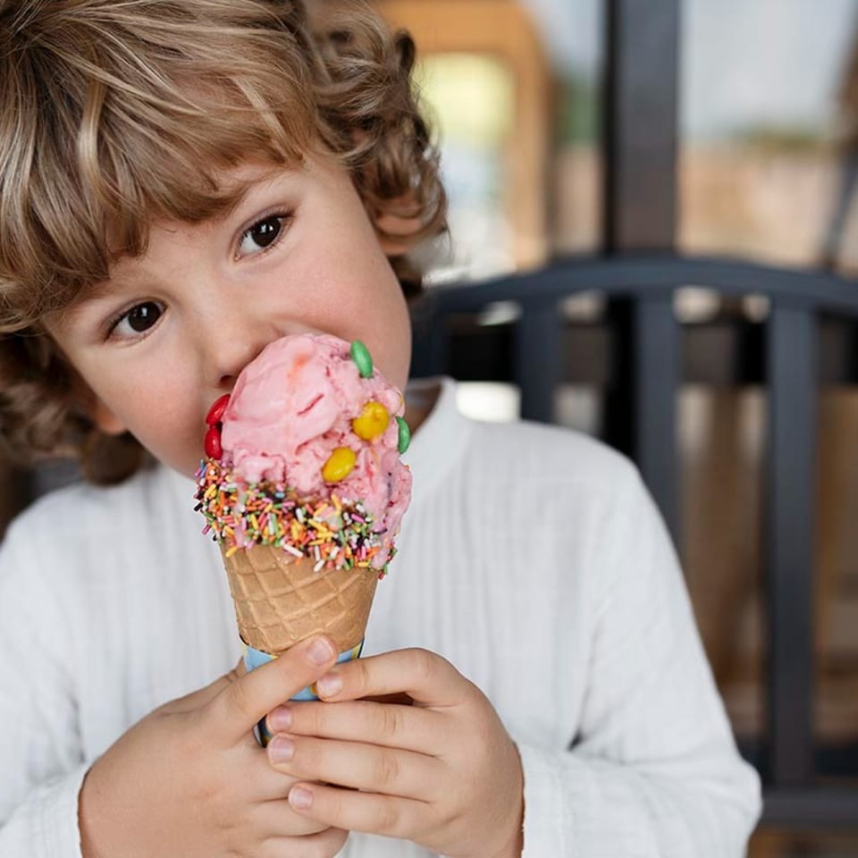 A young boy with curly hair enjoying a pink ice cream cone with colorful sprinkles and candies.