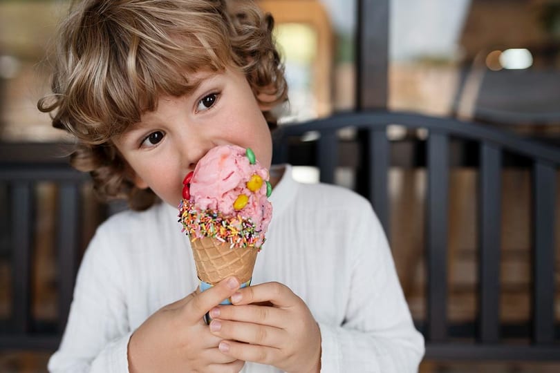 A young boy with curly hair enjoying a pink ice cream cone with colorful sprinkles and candies.