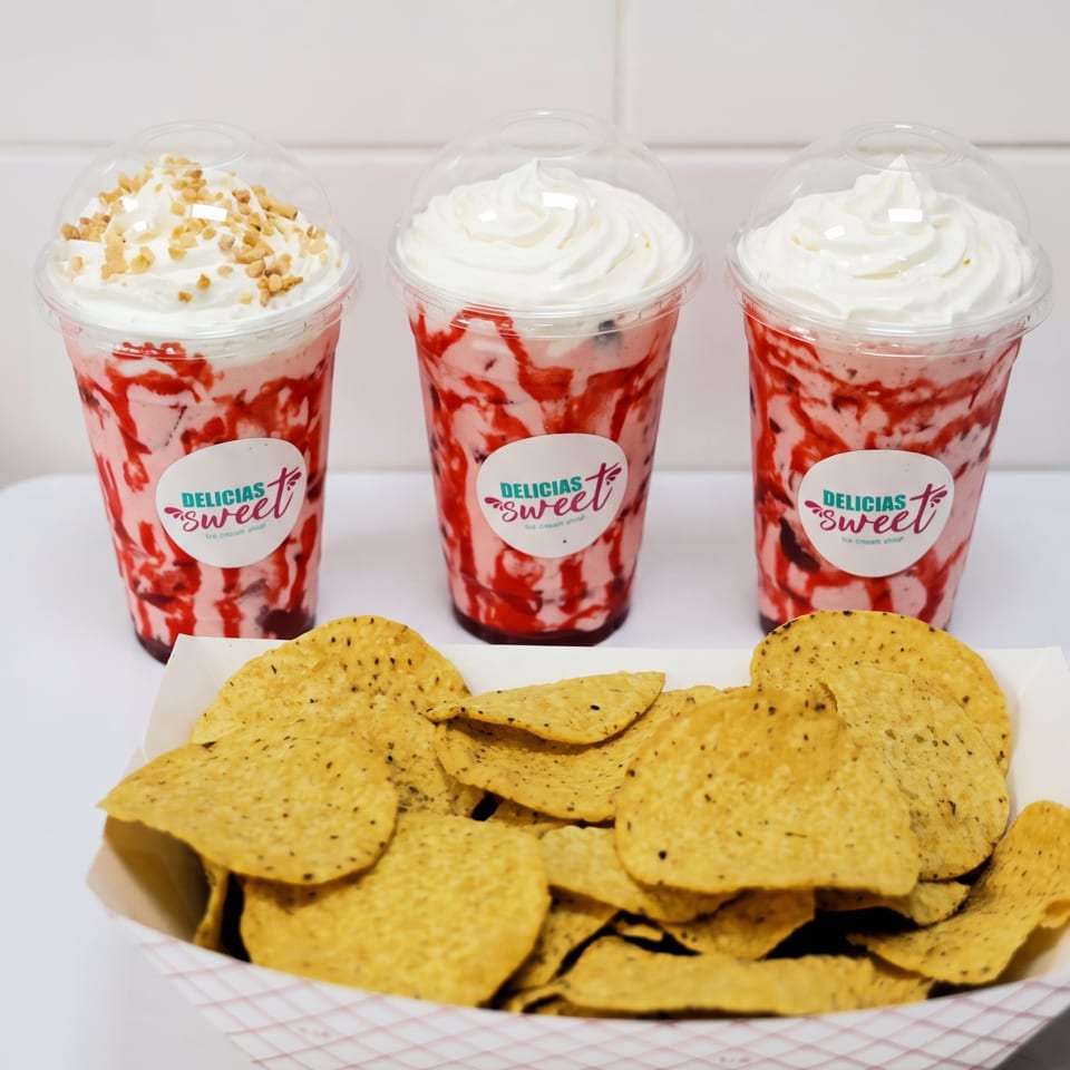 Three Delicias Sweet strawberry milkshakes with whipped cream and a tray of tortilla chips.