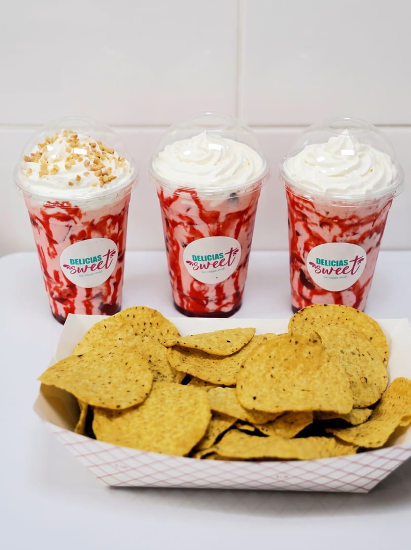Three Delicias Sweet strawberry milkshakes with whipped cream and a tray of tortilla chips.