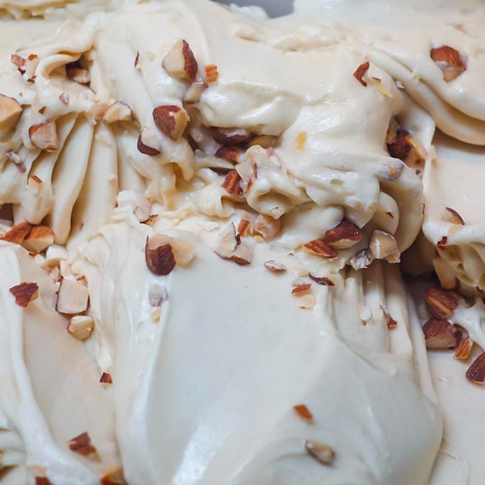 Close-up of creamy, light-colored gelato swirled with scattered chopped almonds.
