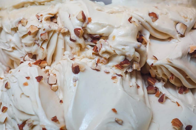 Close-up of creamy, light-colored gelato swirled with scattered chopped almonds.