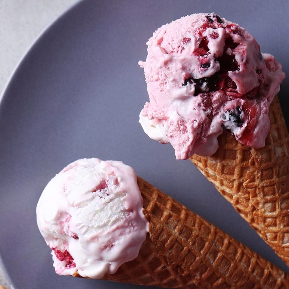 Two waffle cones filled with scoops of pink berry ice cream on a gray plate.