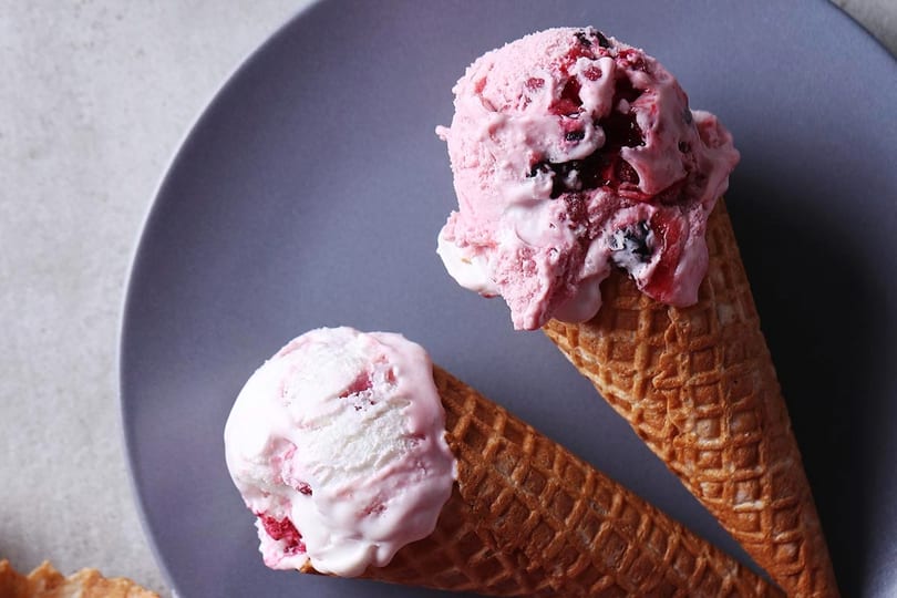Two waffle cones filled with scoops of pink berry ice cream on a gray plate.