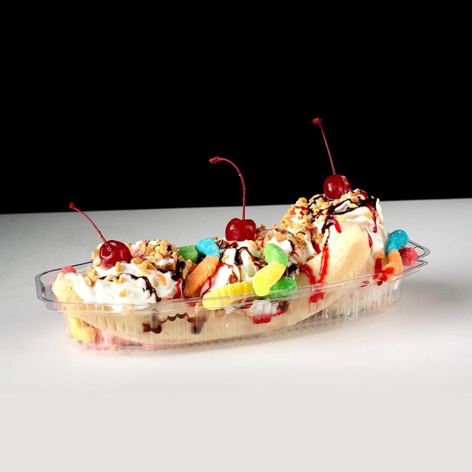 A banana split in a clear plastic dish, topped with whipped cream, cherries, nuts, and gummy candies.