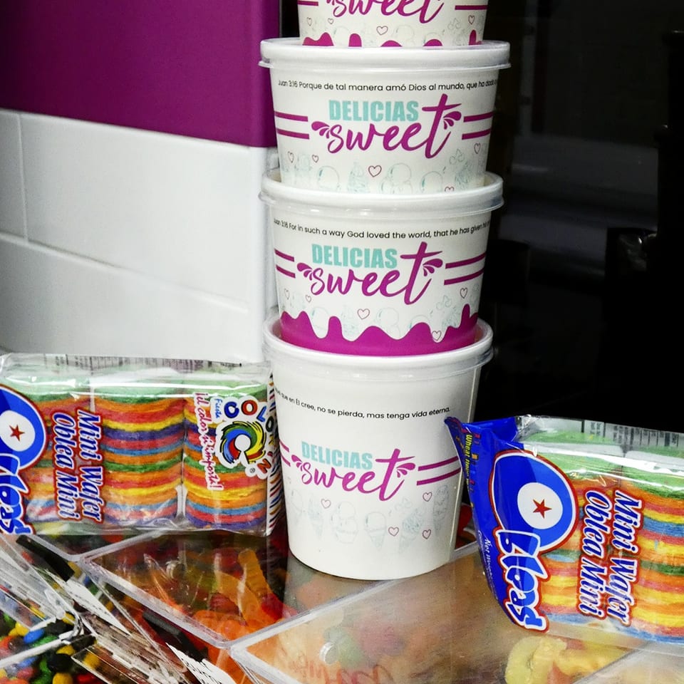 Stacked white and pink "DELICIAS sweet" cups next to colorful mini wafer packages and candy.