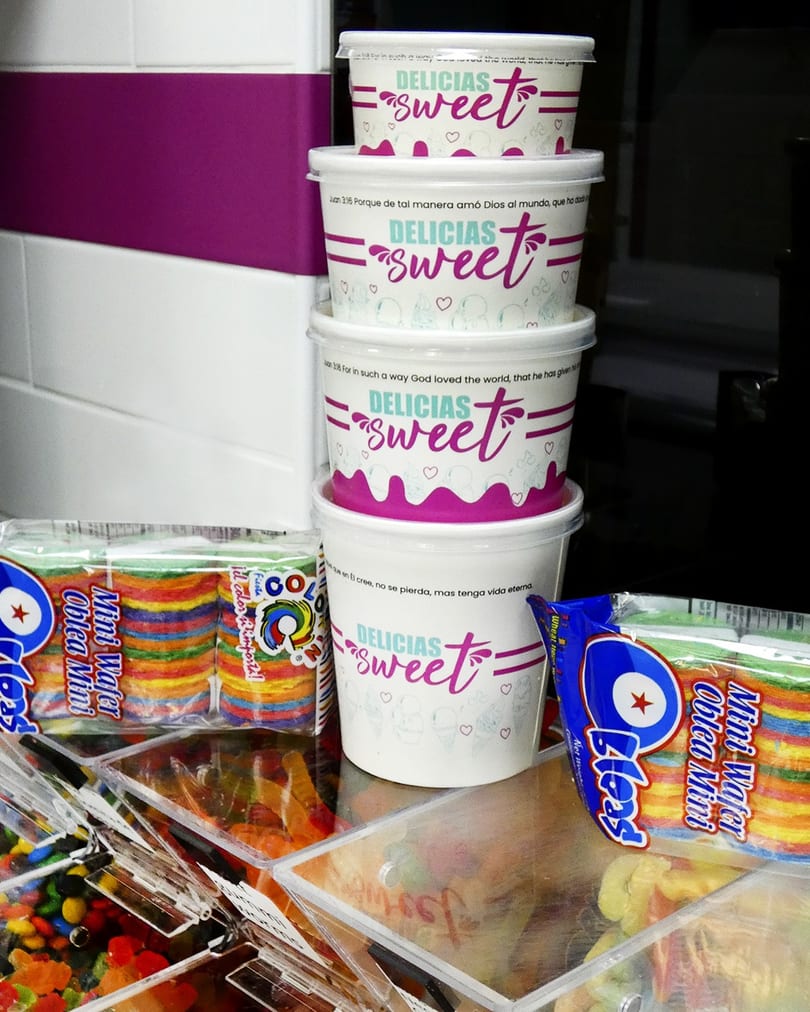 Stacked white and pink "DELICIAS sweet" cups next to colorful mini wafer packages and candy.