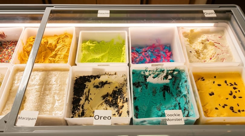 A display case filled with various flavors of ice cream, including pistachio, Oreo, and Cookie Monster.