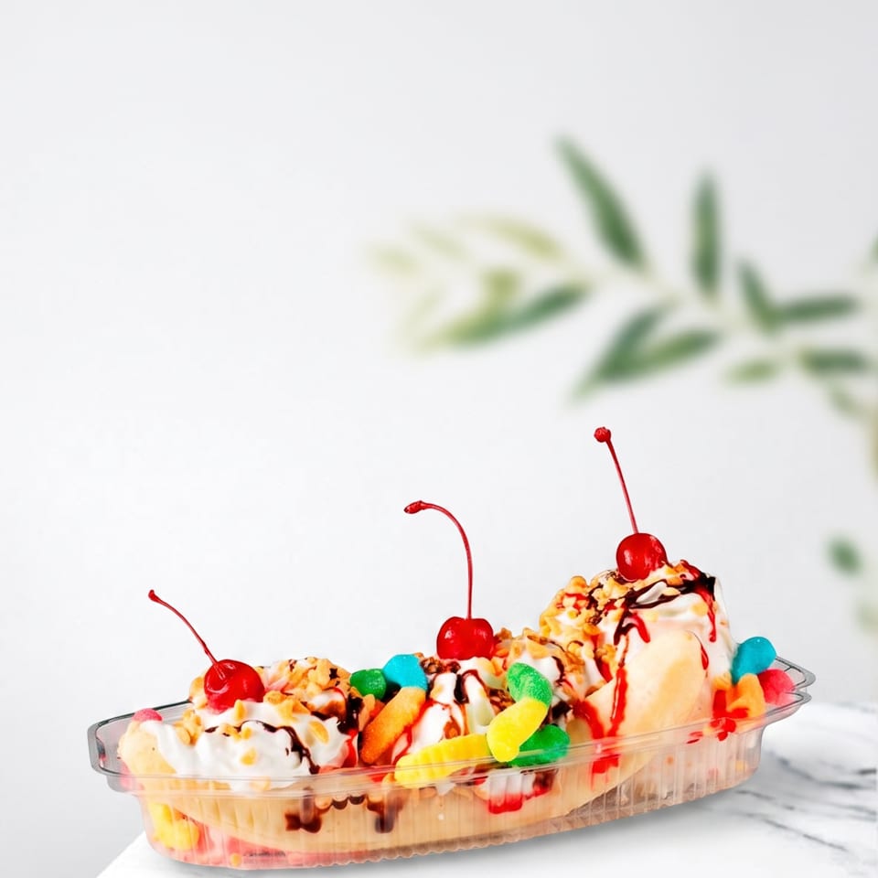 A banana split in a clear dish, topped with whipped cream, cherries, nuts, and gummy candies.