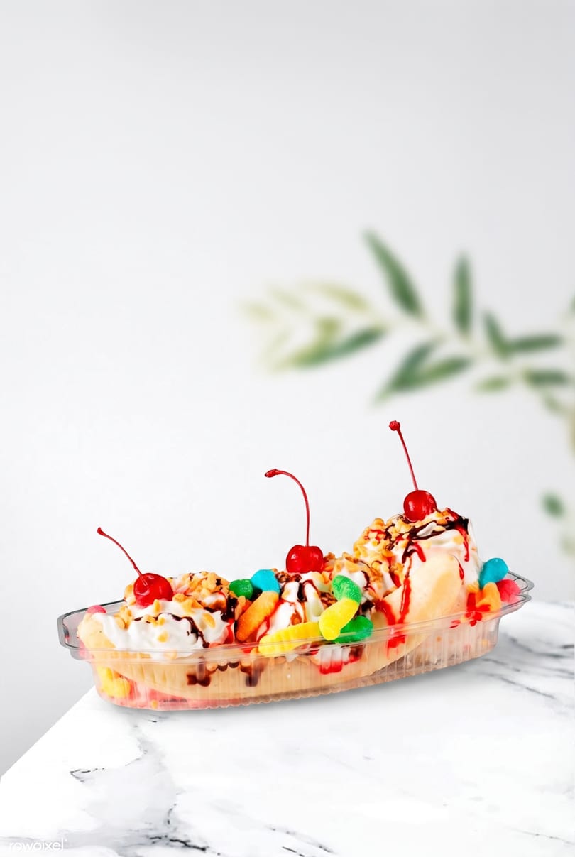 A banana split in a clear dish, topped with whipped cream, cherries, nuts, and gummy candies.