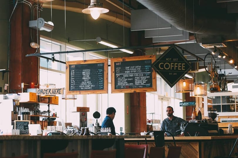 Two men stand behind a coffee shop counter with menus and a "Not Just Coffee" sign hanging above.